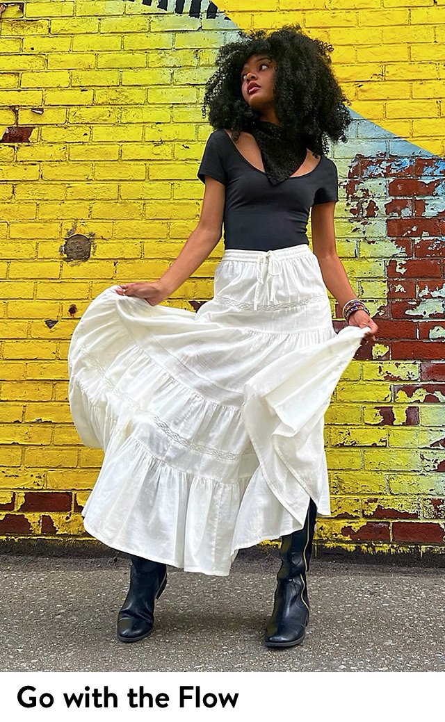 A woman wearing a white maxi skirt, black boots and a scoop-neck T-shirt.