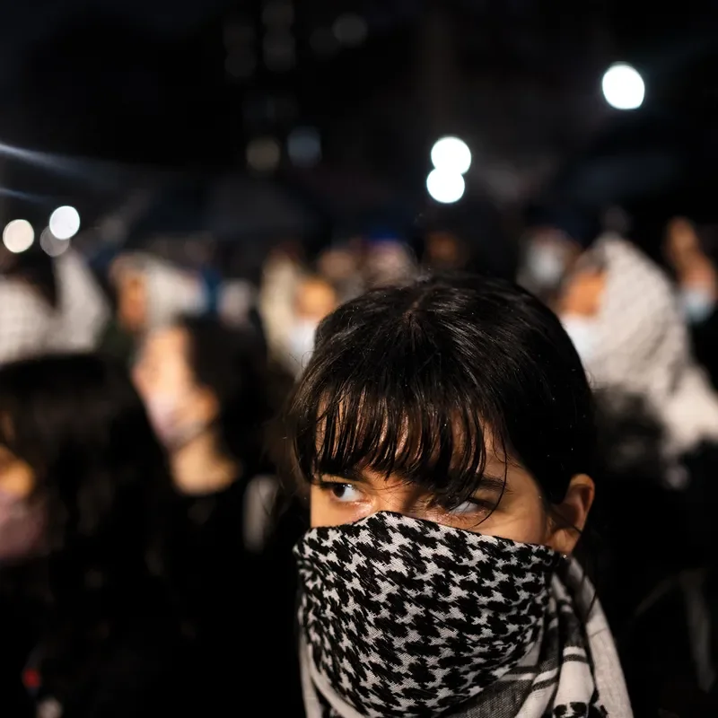 A protester, with their face covered, at night on a college campus.