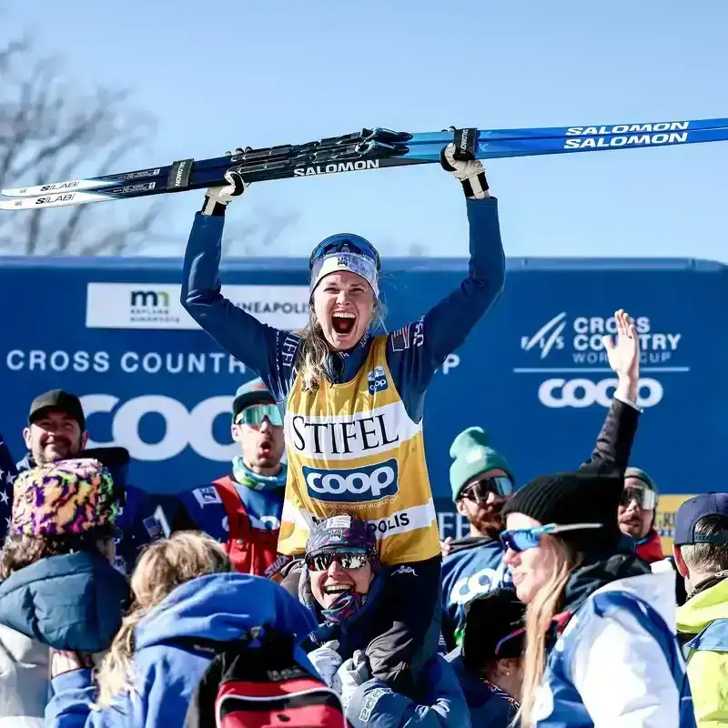 A person holding up skis while celebrating.