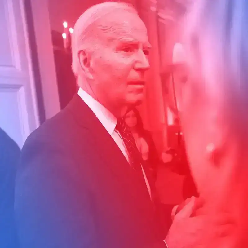 U.S. President Joe Biden at an event in a group of people. There is a blue and red tinted overlay on the image. 