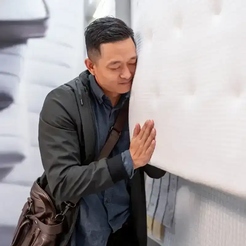 A man puts his face to a mattress hanging from the ceiling in a mattress store. 