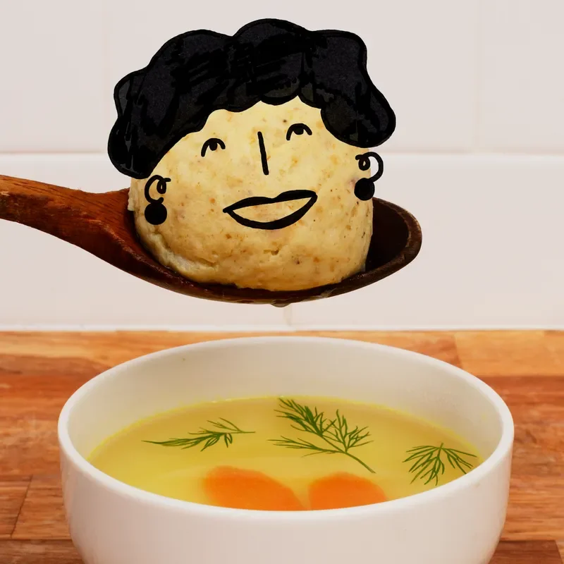 A face drawn on a matzo ball above a bowl of soup.