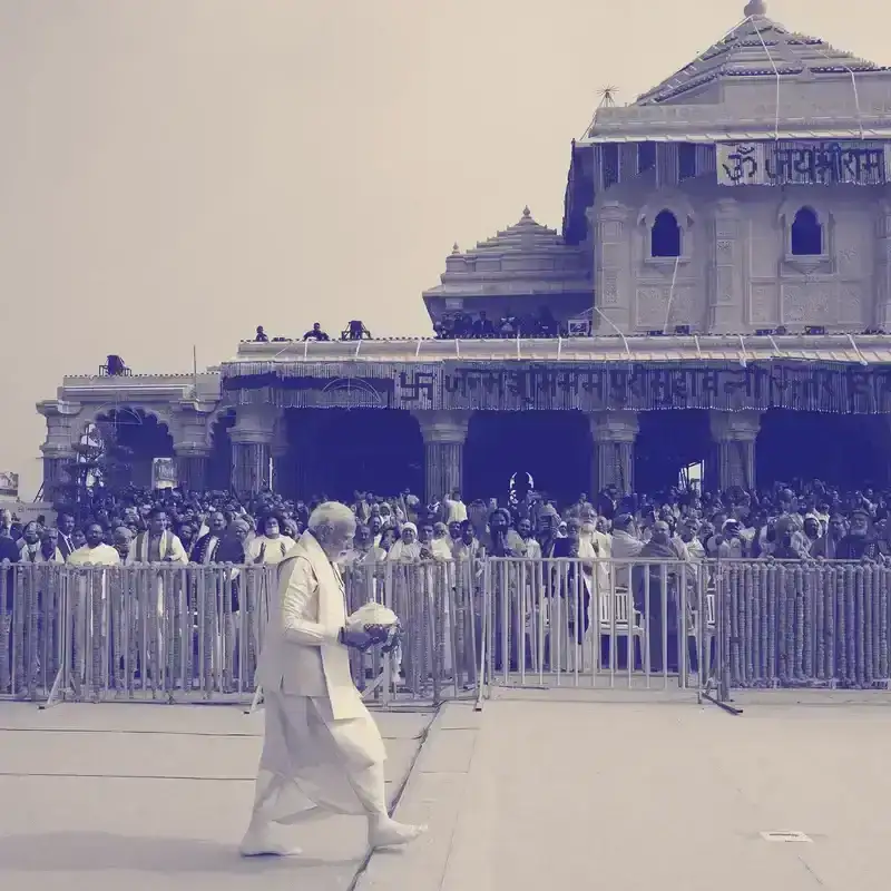 Indian Prime Minister Narendra Modi walking in front of a crowd of people at a temple opening in Ayodhya, India. Modi is wearing all-white clothing, and is holding something in his hands. There is a blue tinted overlay treatment on the image. 