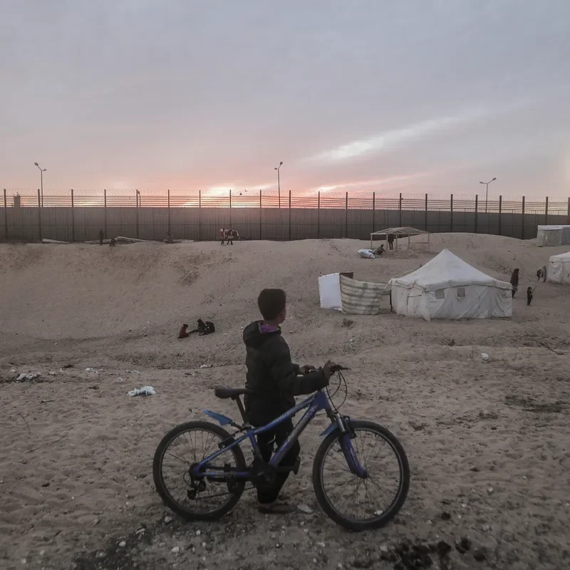 A child stands with a bicycle in Rafah looking at the border wall separating Egypt and Gaza. 
