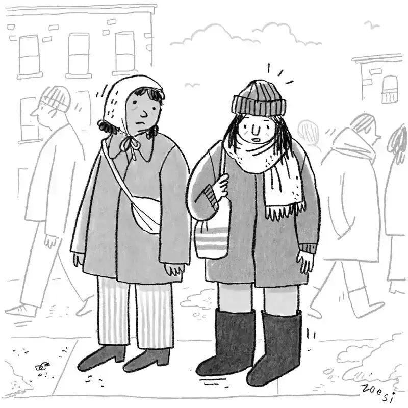 Two people in a street are wearing winter clothing. 
