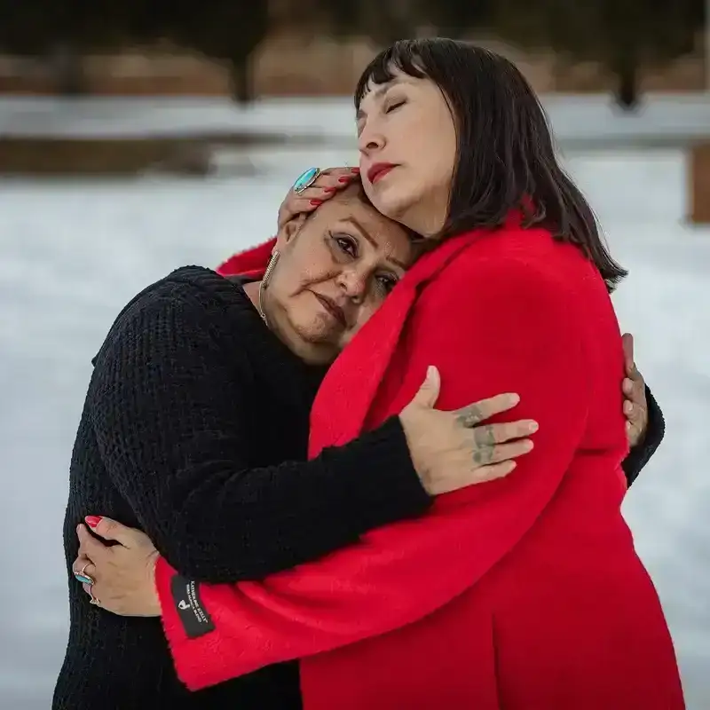 Two women embracing in a snowy landscape.