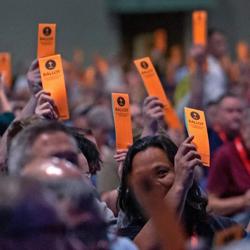 People holding bright orange ballots in the air at the 2024 Southern Baptist Convention.